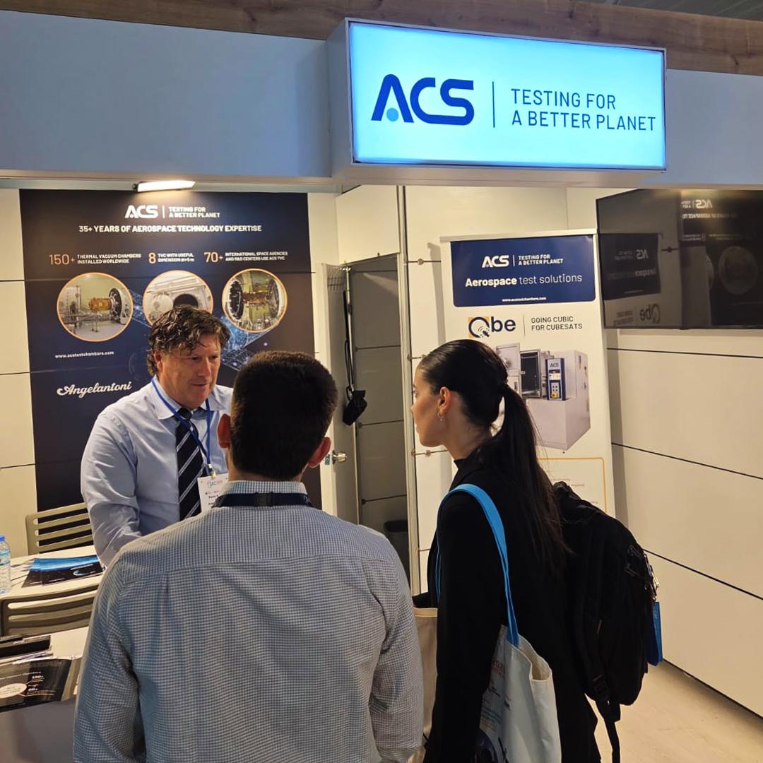 Un représentant d'ACS Angelantoni Test Solutions échange avec deux visiteurs sur le stand d'exposition lors de l'International Astronautical Congress (IAC).